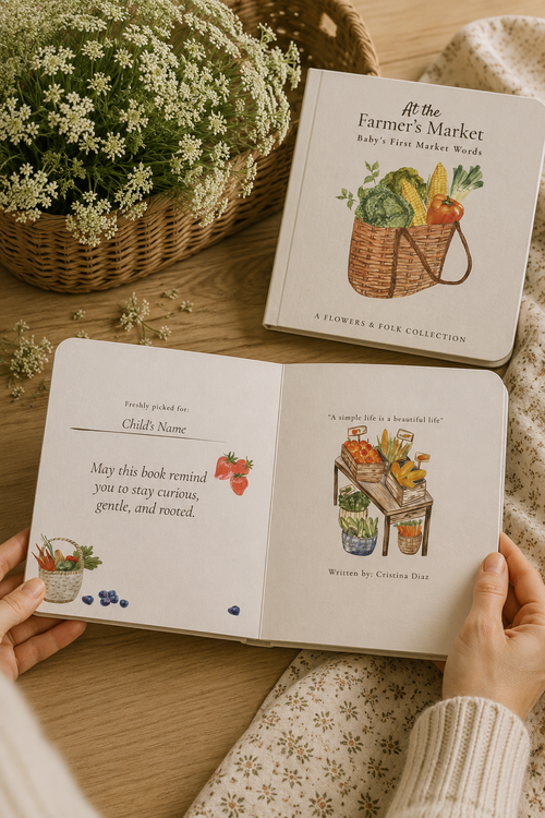 A person holds an open personalized children's book titled 'It's the Farmer's Market' from The Farmer's Market series, with a matching closed book placed above it on a wooden surface. The pages show illustrated produce and grocery scenes, and the scene includes a wicker basket of flowers and a cream floral blanket.